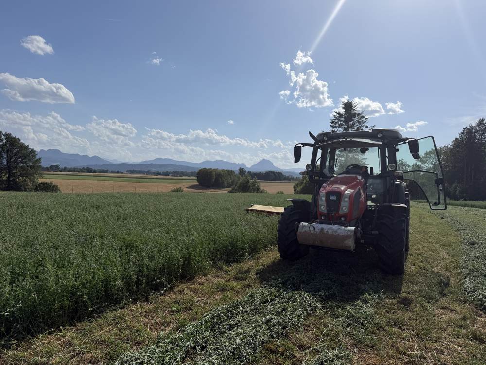 Traktor beim Mähen vor Bergpanorama
